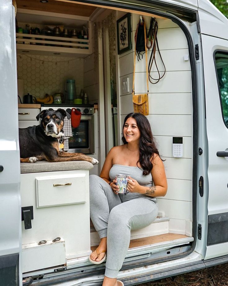 a woman sitting in the back of a van next to a dog and holding a cup