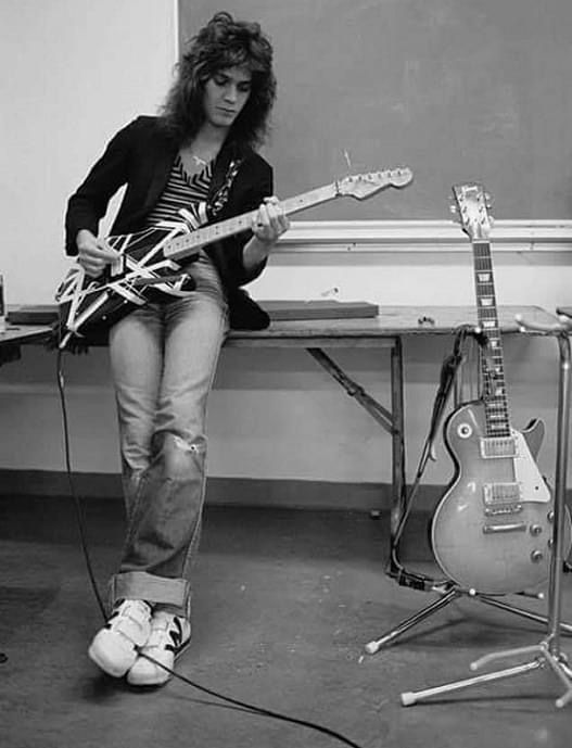 a woman sitting in front of a blackboard with two guitars on her lap and another guitar next to her