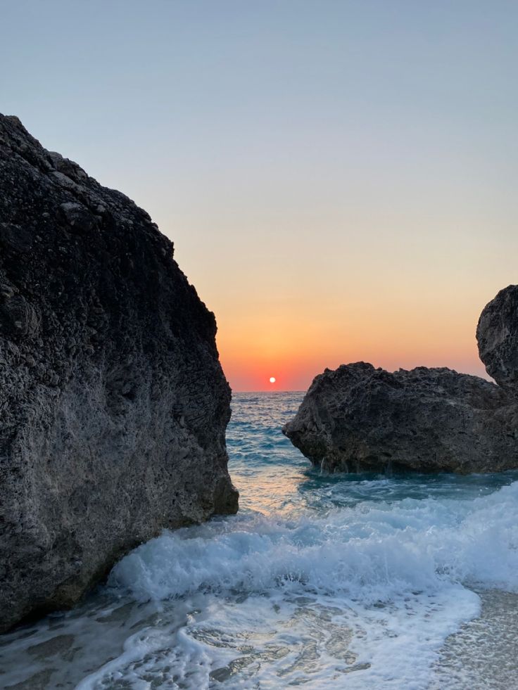 the sun is setting over the ocean and rocks