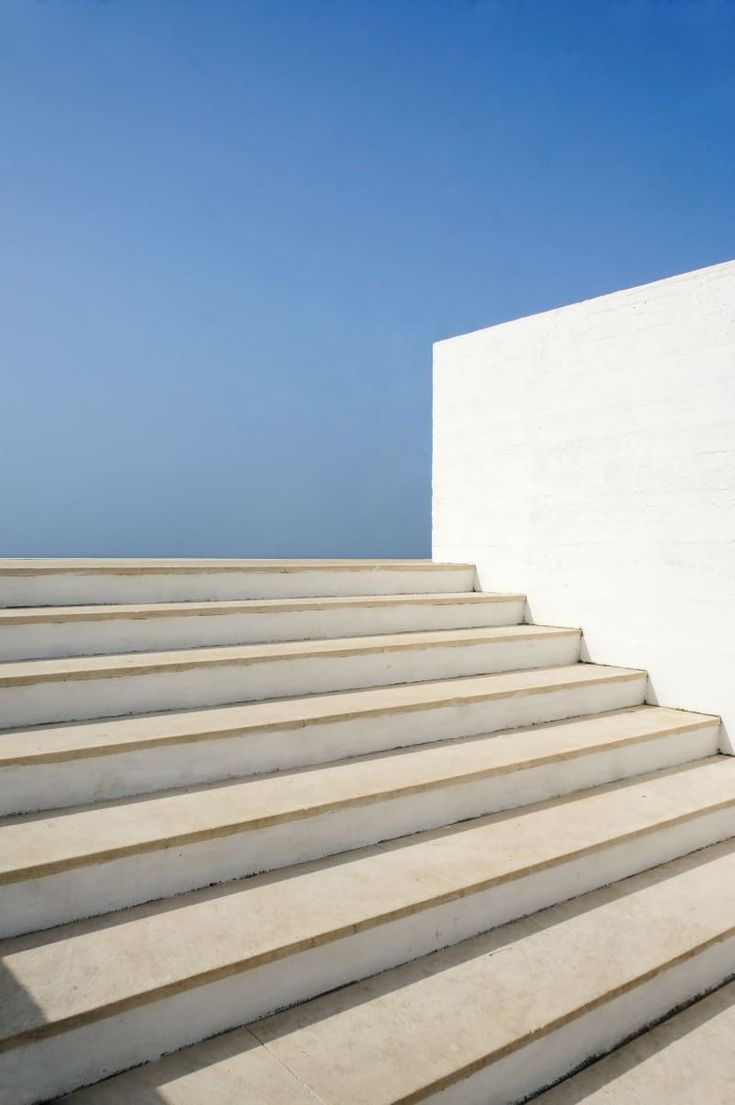 there is a white building with steps leading up to the sky and blue water in the background