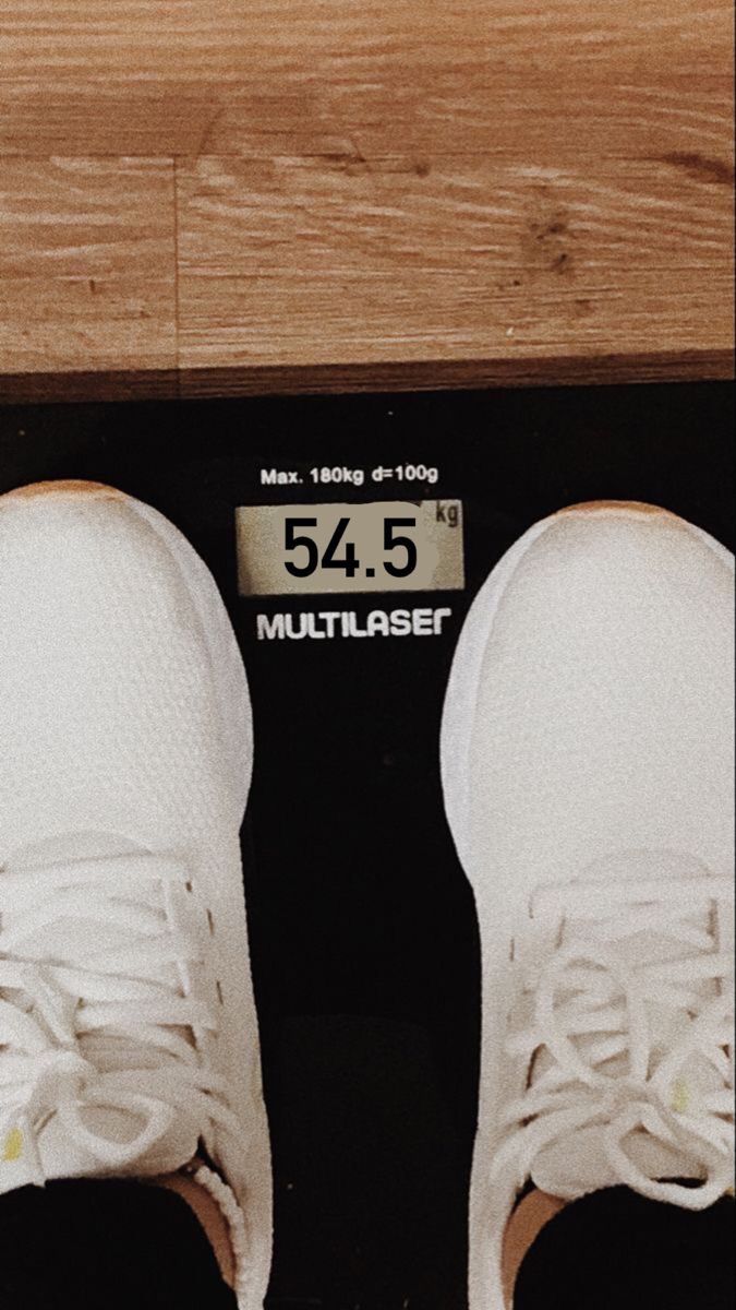 a pair of white shoes sitting on top of a black scale next to a wooden floor