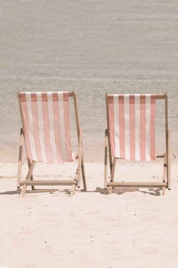 two beach chairs sitting on top of a sandy beach next to the ocean with water in the background