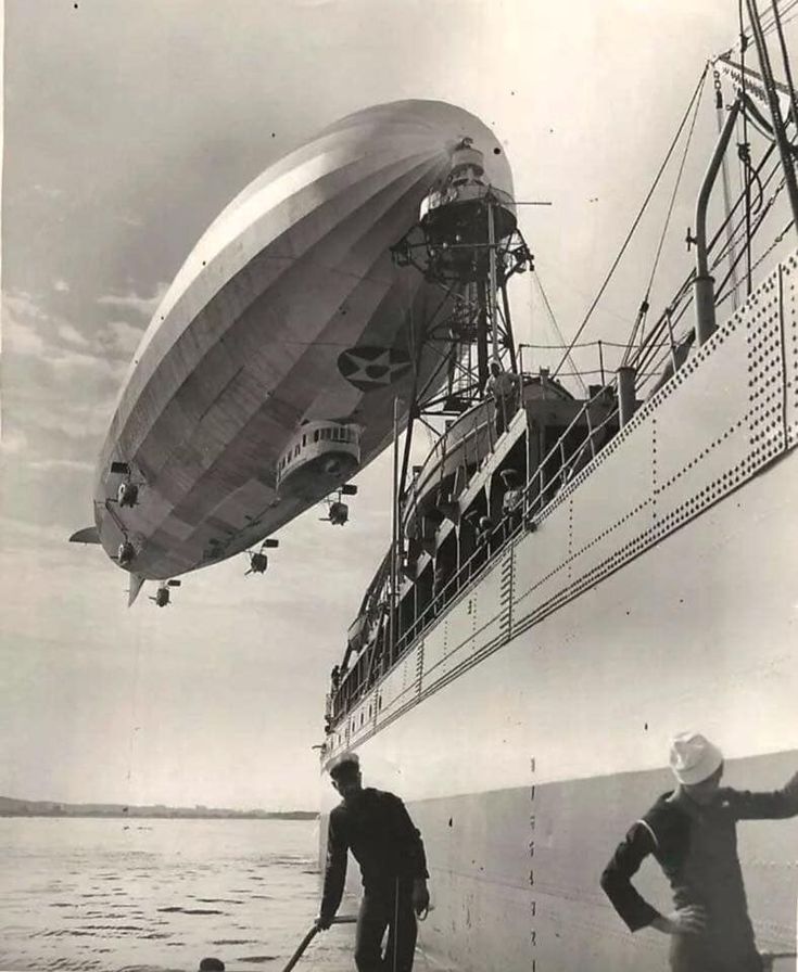 two men standing next to each other in front of a large boat