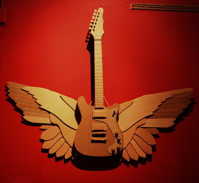 an image of a guitar with wings cut out of it's body on a red wall