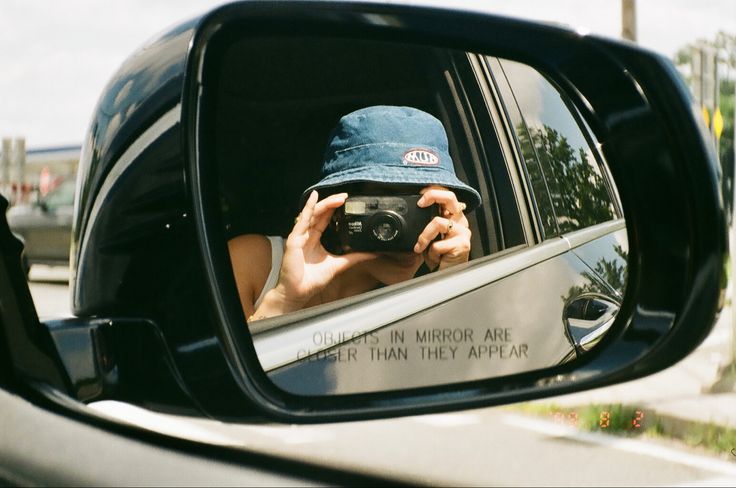 a person taking a photo in the side mirror of a car while holding a camera