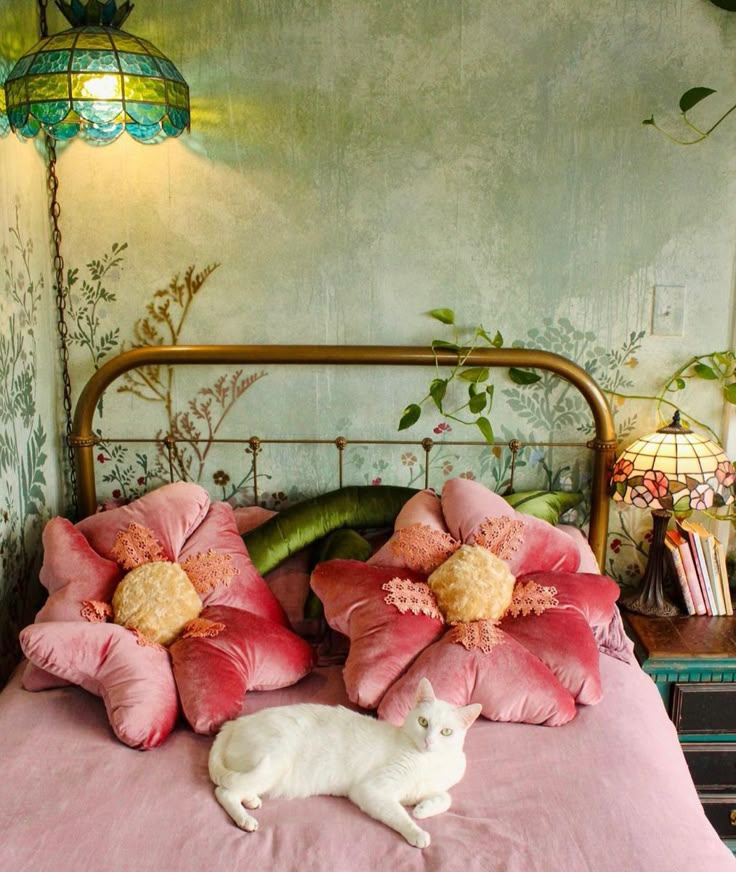 a white cat laying on top of a bed next to pink pillows and flower decorations