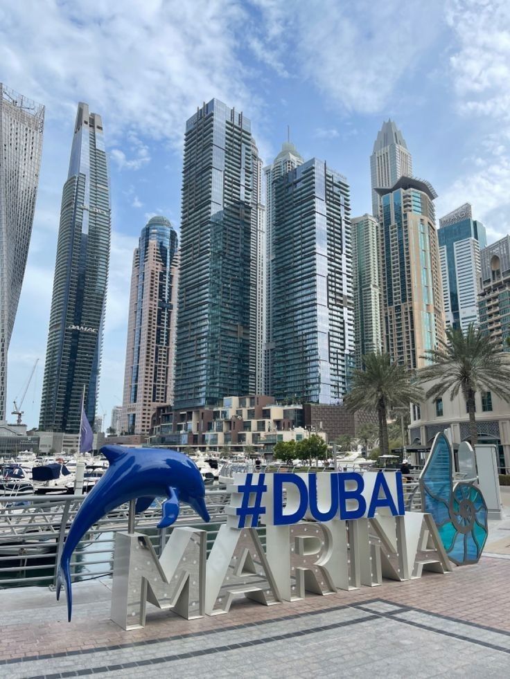 a sign that says dubai marina in front of some tall buildings and a dolphin statue