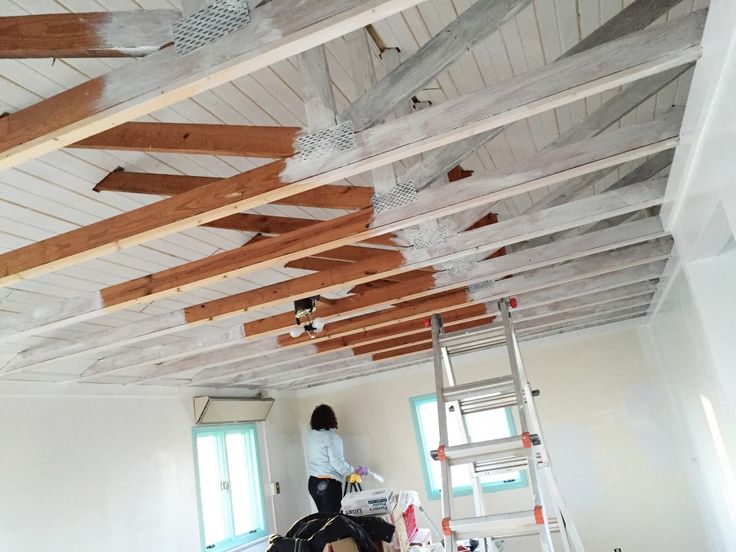 a woman standing on a ladder in a room with unfinished wood ceilinging and white walls