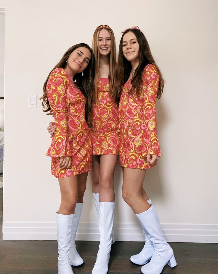 three young women standing next to each other in front of a wall wearing white boots