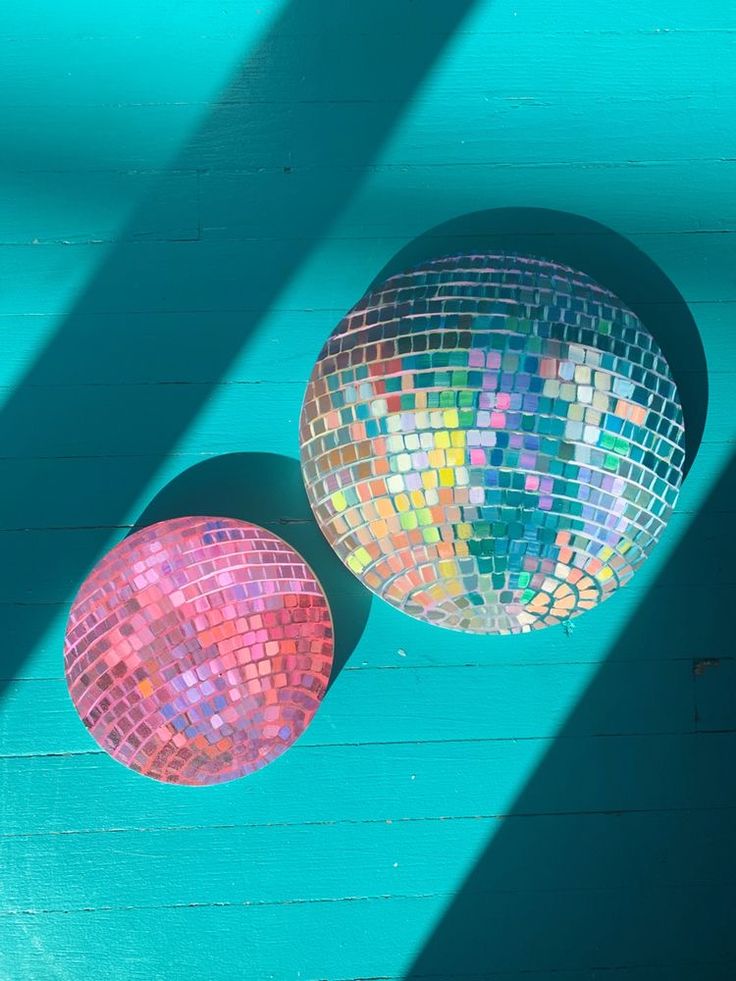 two disco balls sitting next to each other on top of a blue wall with shadows