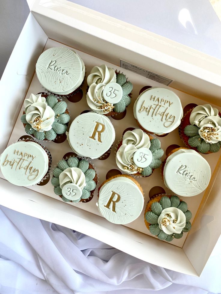 twelve cupcakes with white frosting and green leaves are in a gift box