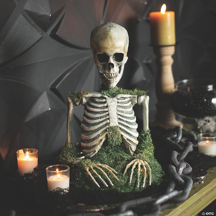 a fake skeleton sitting in the middle of a table with candles and moss on it