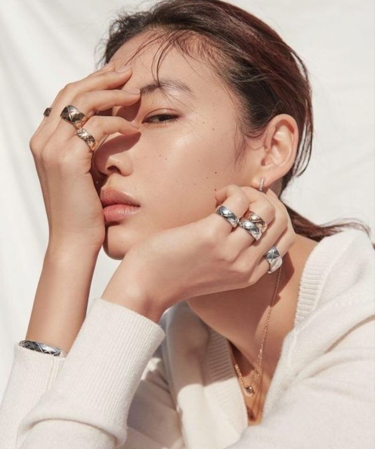 a woman with rings on her fingers is posing for the camera while wearing a white sweater