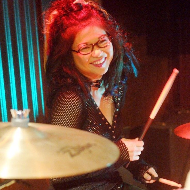 a woman with red hair and glasses playing drums