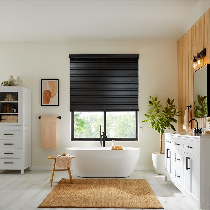 a white bath tub sitting in a bathroom next to a window with black roller shades