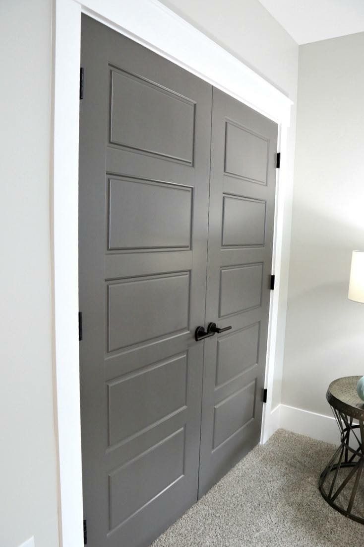 a gray door in a white room next to a table with a lamp on it