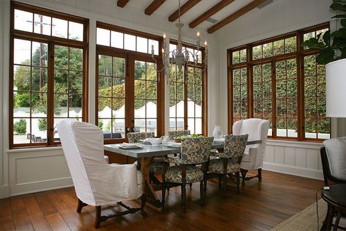 a dining room table with white chairs and wooden flooring in front of large windows