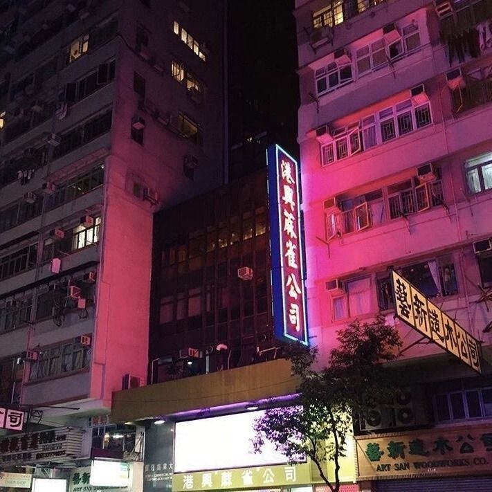 the buildings are lit up at night with neon lights on them and people walking by