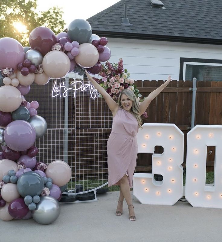 a woman standing in front of a large balloon arch with the number 30 on it