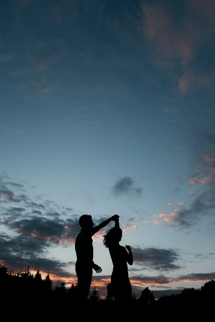 a man and woman standing next to each other under a cloudy blue sky at sunset