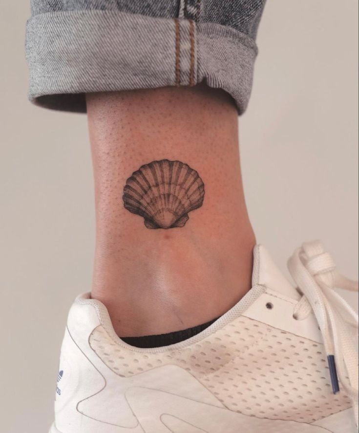 a woman's foot with a small shell tattoo on the side of her ankle