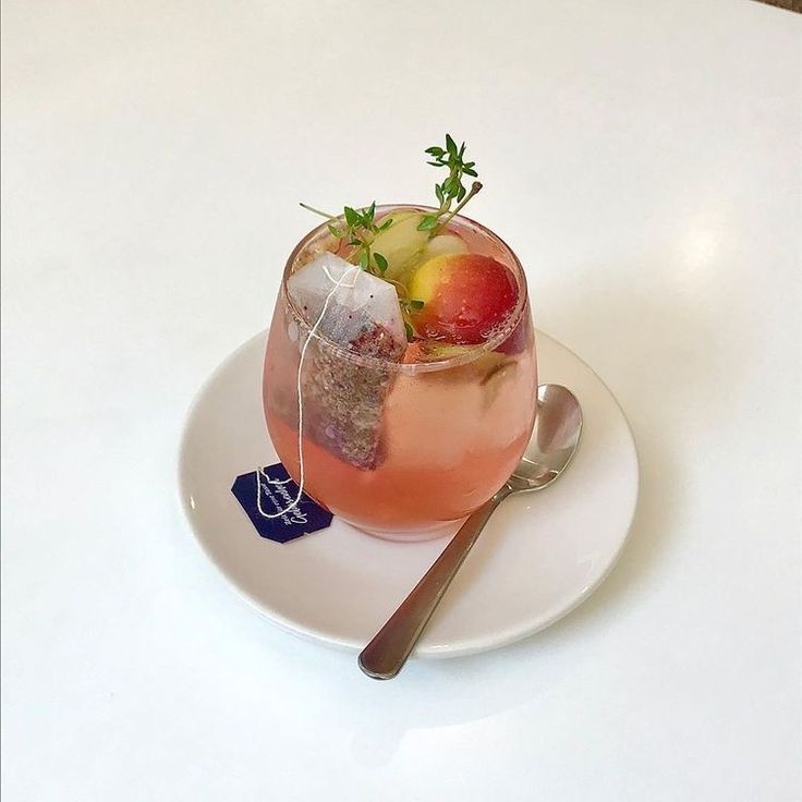 a glass filled with fruit and ice on top of a white plate next to a spoon