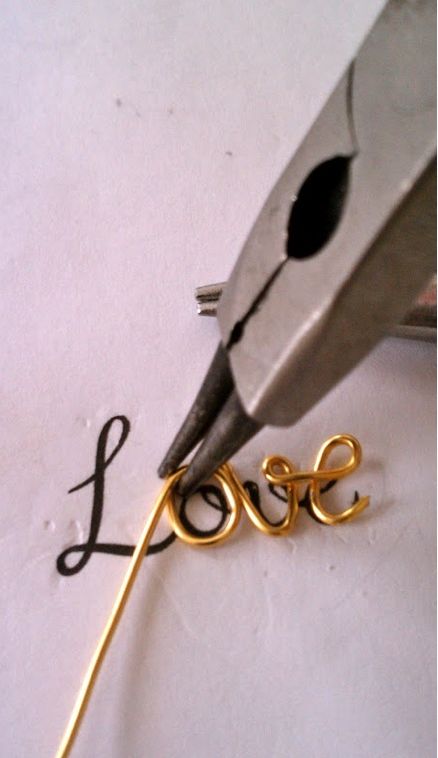 a pair of scissors cutting the word love out of paper with gold colored metal wire