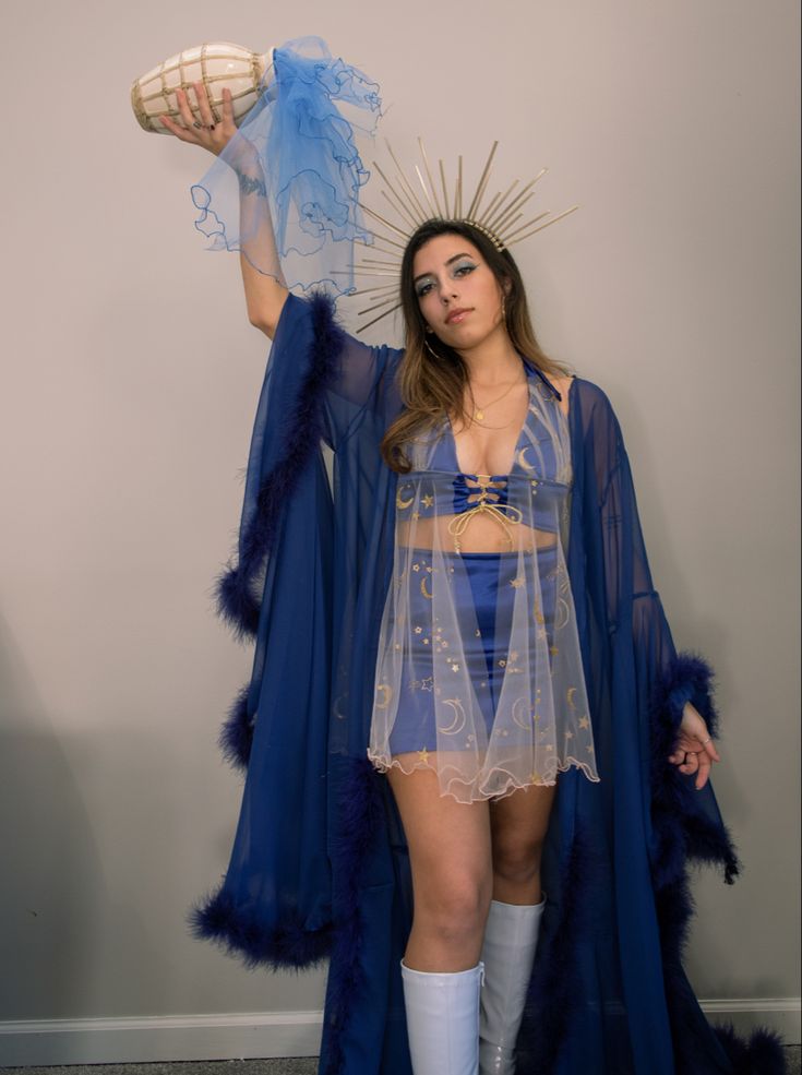 a woman dressed in blue is posing with her hands behind her head and holding a fan