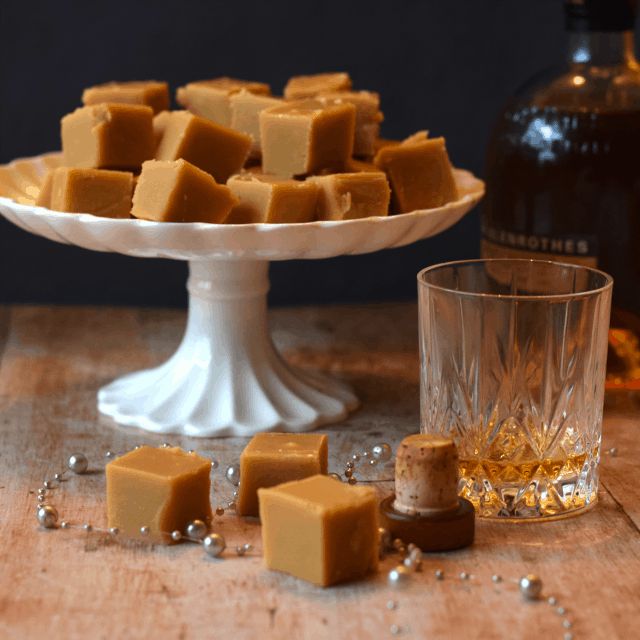 several pieces of caramel fudge sitting on a table next to a glass and bottle