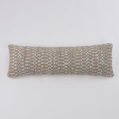 a long rectangular pillow on a white wall with a brown and tan checkerboard pattern