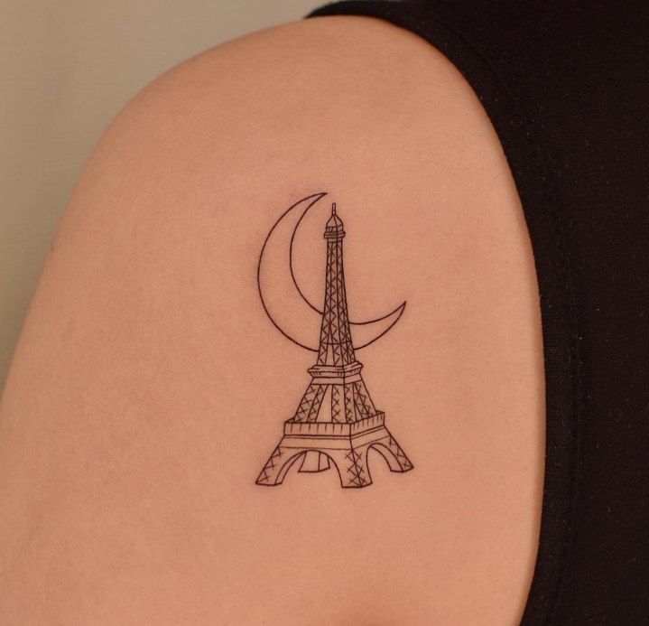 the back of a woman's shoulder with a small tattoo of the eiffel tower