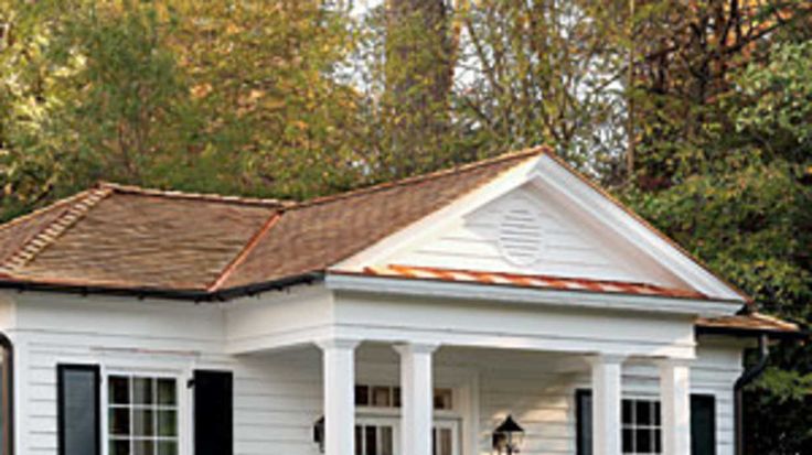 a small white house with black shutters on the front and side windows, surrounded by trees