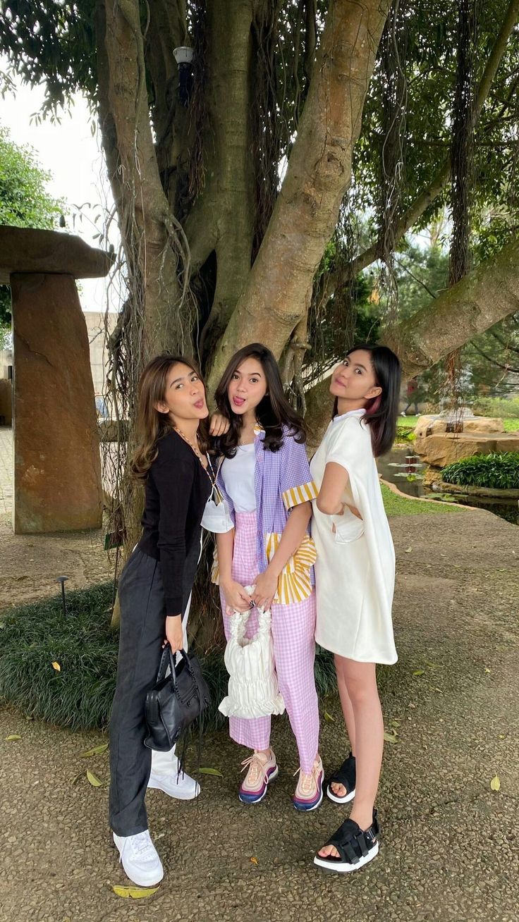 three young women standing next to each other under a tree in front of a statue