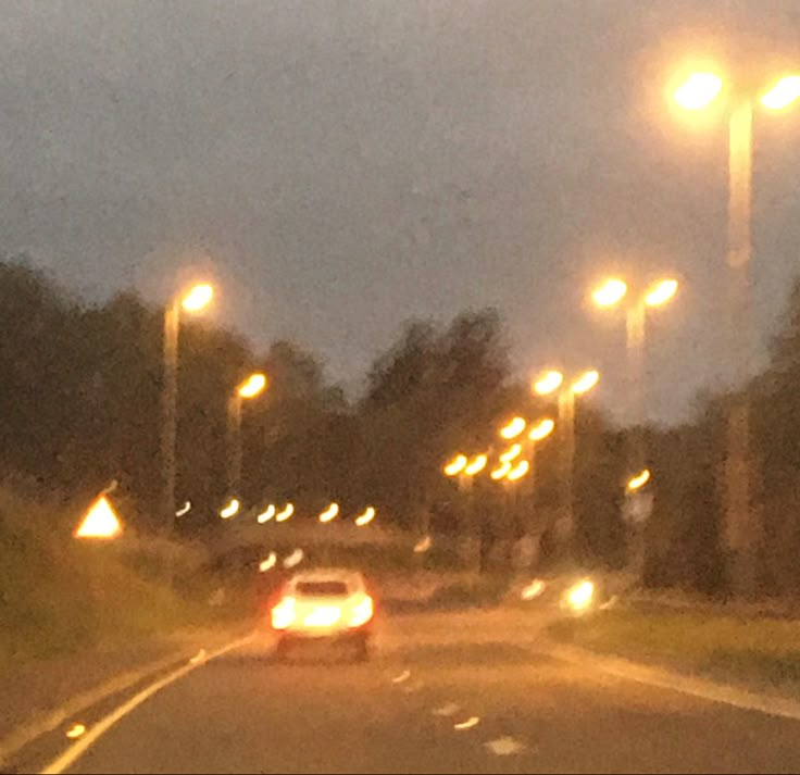 the car is driving down the road at night with street lights on either side of it