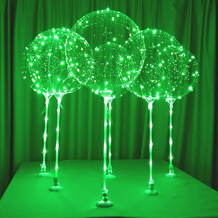 three green lighted trees on top of a table with lights in the shape of balls