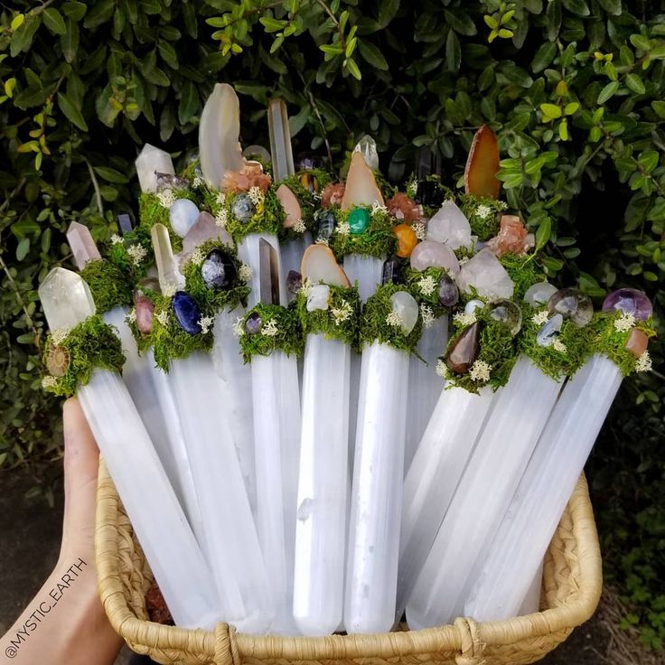 a basket filled with lots of white candles covered in green plants and rocks on top of each other