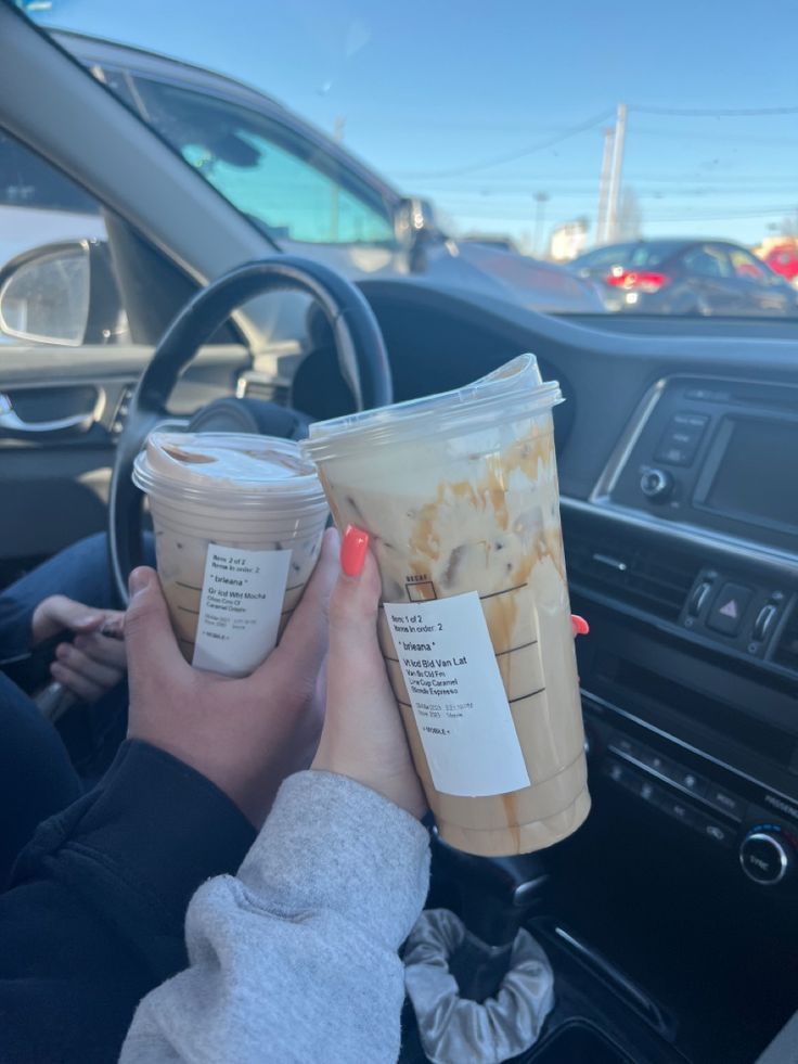 two cups of coffee are being held up in the drivers seat of a car while someone is driving