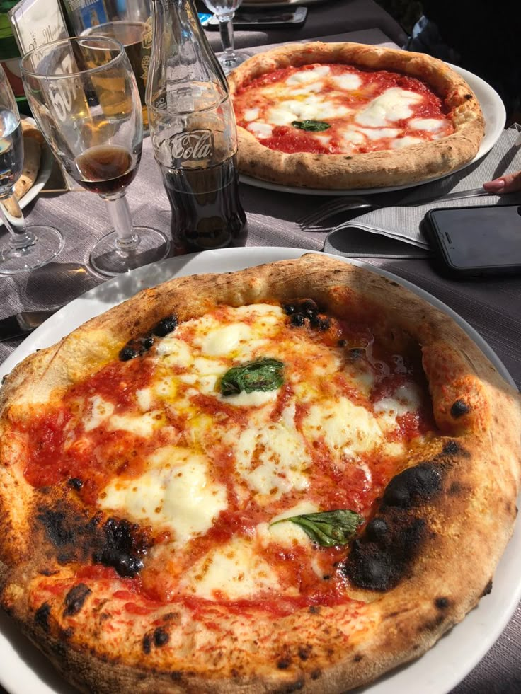 two pizzas sitting on top of white plates next to glasses of water and silverware