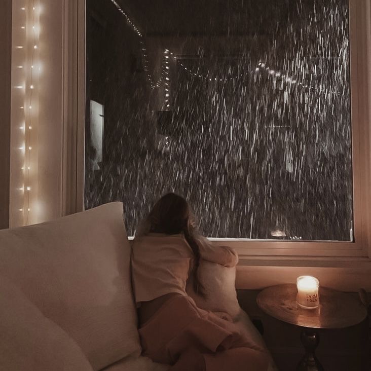 a woman sitting on a couch in front of a window with rain falling down the outside