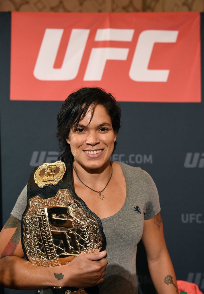 a woman holding a gold and black wrestling belt in front of a sign that says ufc