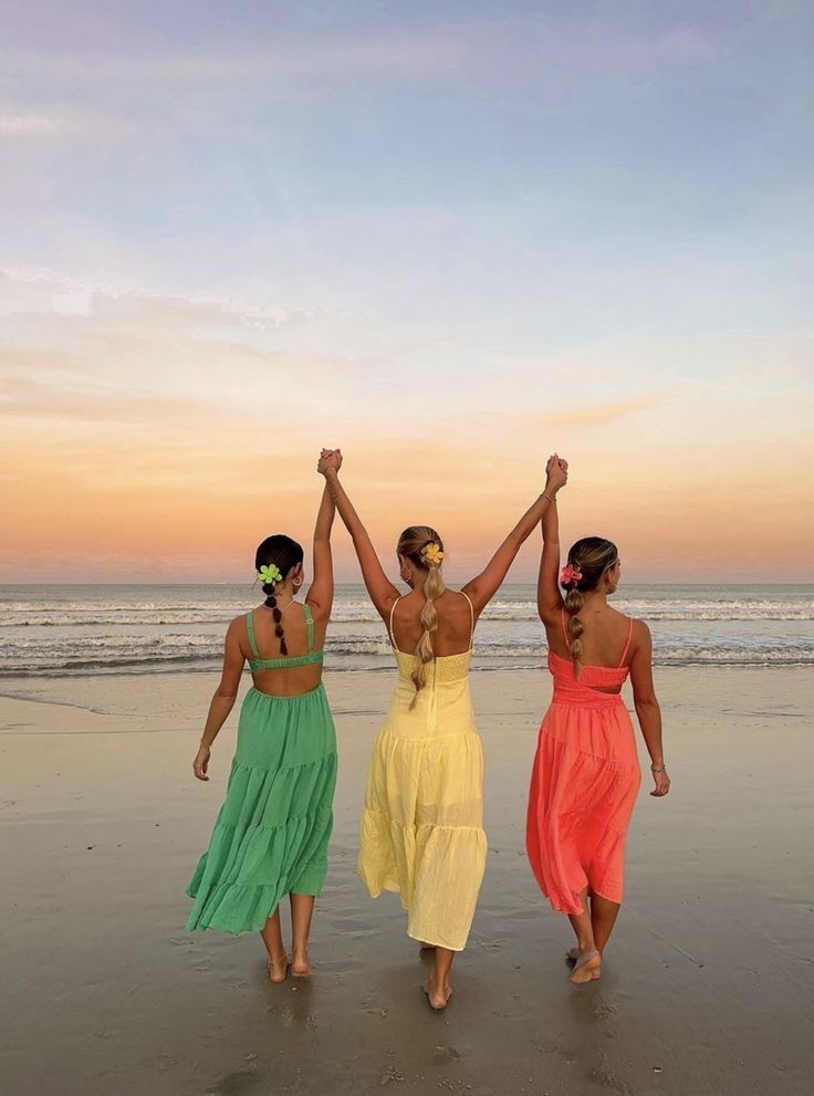 three women walking on the beach with their arms in the air