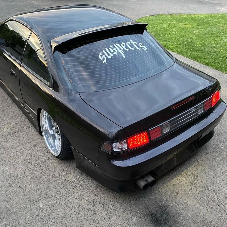 the back end of a black sports car parked in front of a driveway with grass