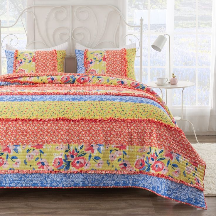 a bed with colorful bedspread and pillows on top of it in front of a window