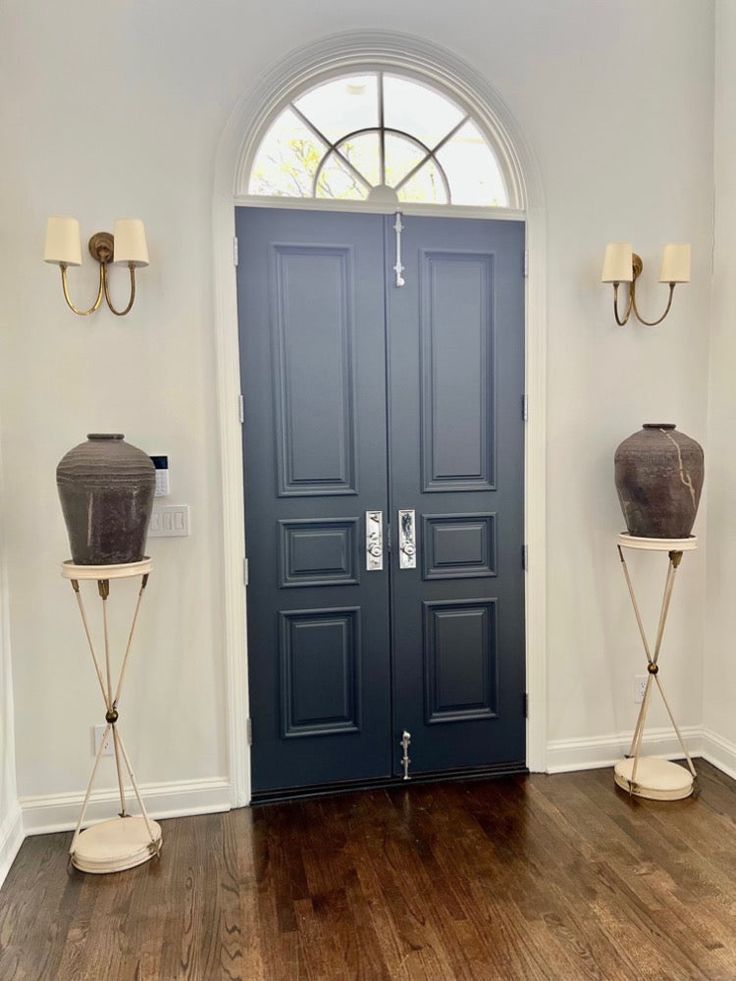 two vases sitting on stands in front of a blue door with arched glass windows