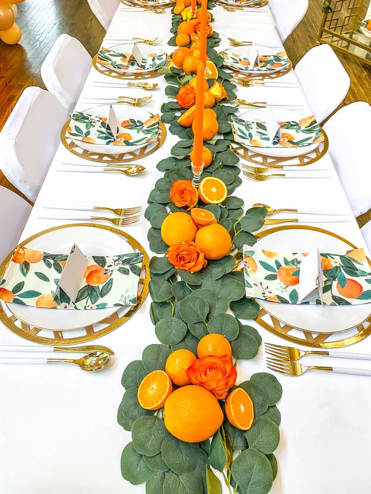 a long table is decorated with oranges and greenery