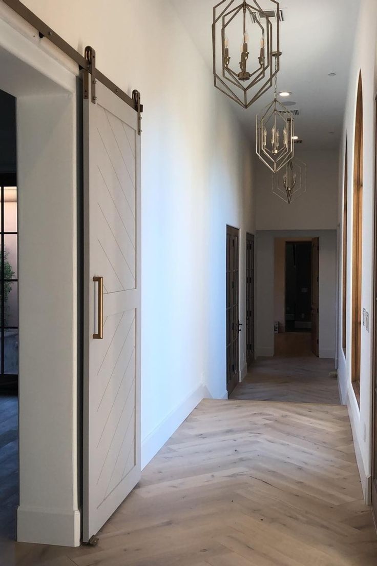 an empty hallway with wooden flooring and chandelier hanging from the ceiling above