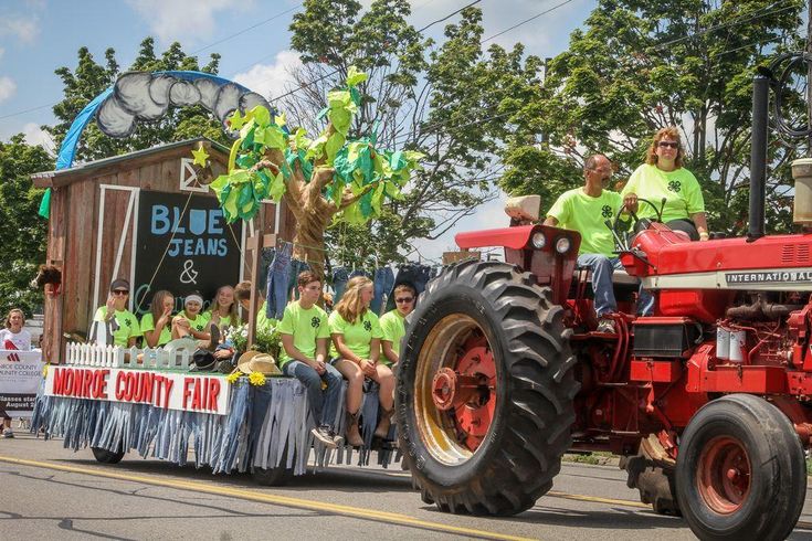 people riding on the back of a red tractor down a street in front of a crowd