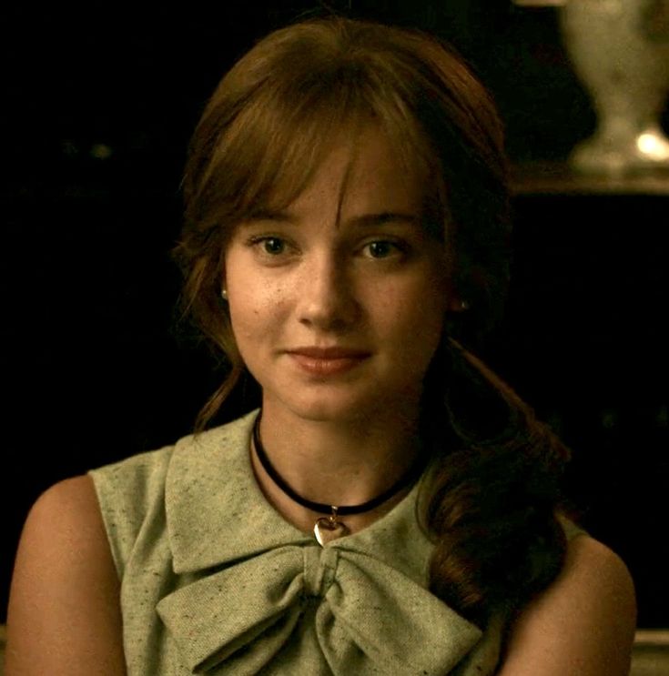 a woman with long hair wearing a green shirt and black necklace sitting in front of a table