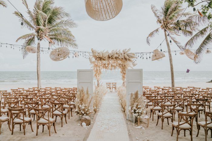 an outdoor ceremony set up on the beach with palm trees and hanging lanterns above it