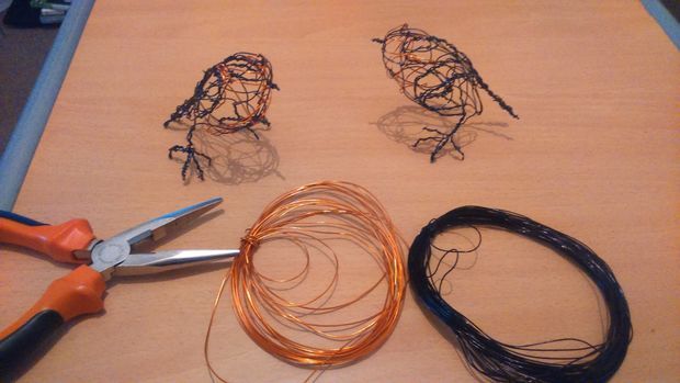 several wire birds sitting on top of a wooden table next to scissors and wires,